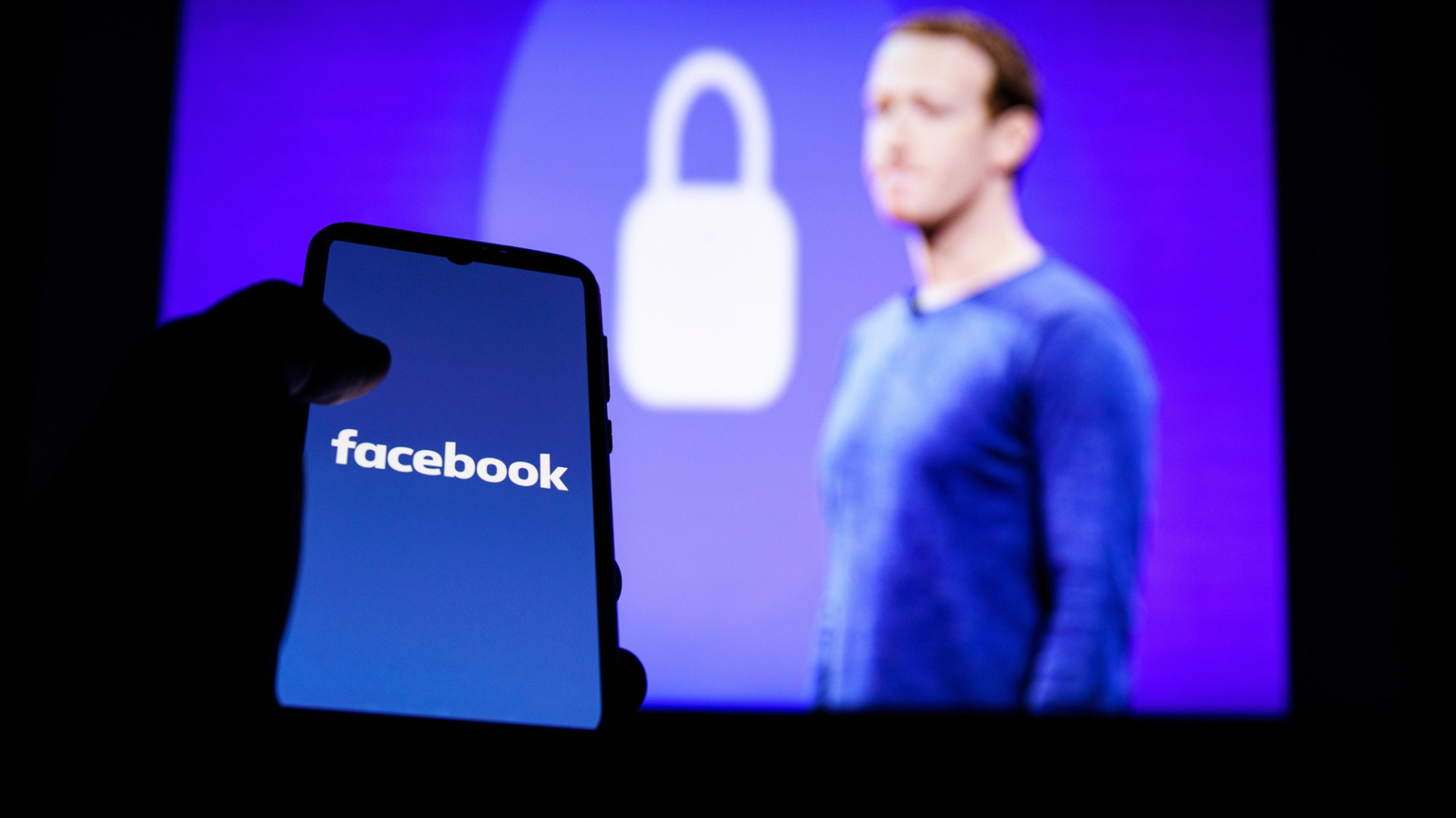 person som håller i en telefon med facebooklogotypen och mark zuckerberg i bakgrunden